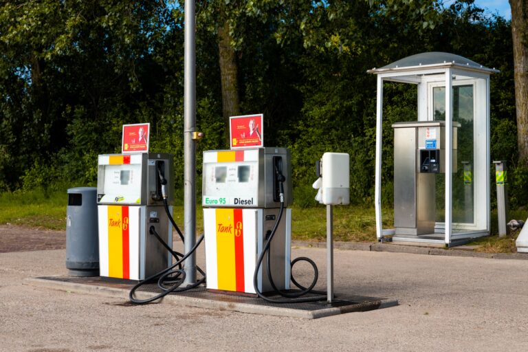 Twee brandstofpompen voor Euro 95 en Diesel bij een tankstation, met betaalautomaat en afvalbak, op een locatie omgeven door bomen.