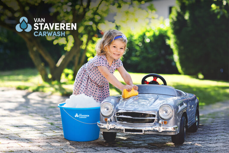 Kind wast speelgoedauto met spons en sopemmer met Van Staveren Carwash-logo – speelse promotie voor autowasservice.