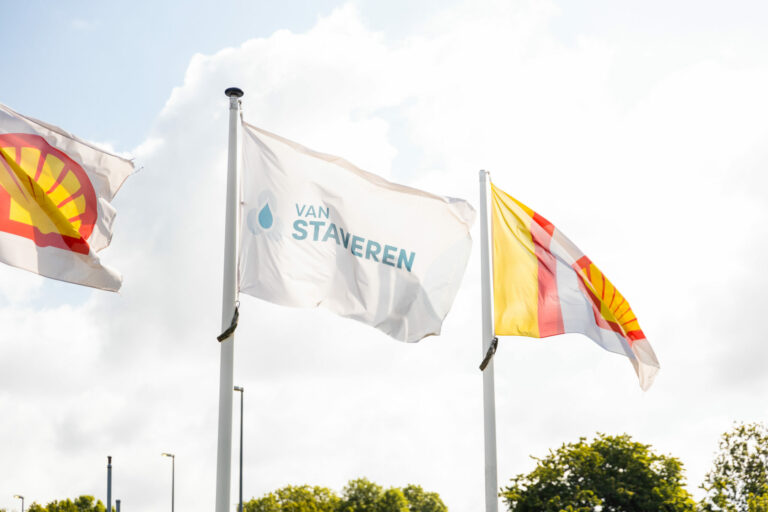 Vlaggen van Van Staveren en Shell wapperend in de wind tegen een heldere lucht.
